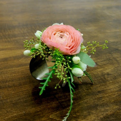 Floral corsage on a cuff bracelet with pink flower and greenery on a wooden surface