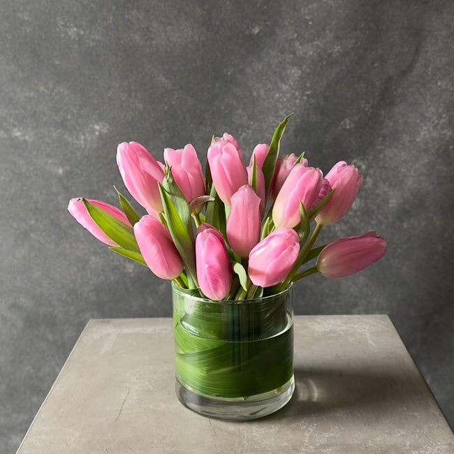 Bouquet of pink tulips in a clear vase on a gray surface with a gray background
