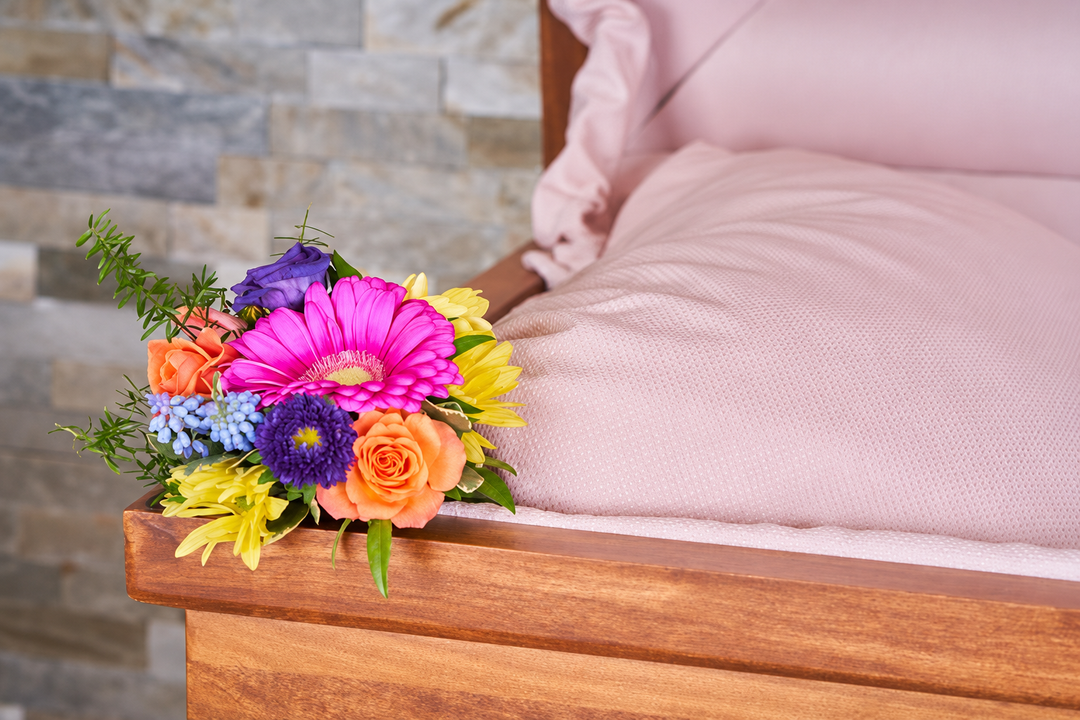 Pink gerbera, peach roses, yellow flowers, pale blue hydrangea, purple blooms, and greenery placed beside the lining inside a casket.