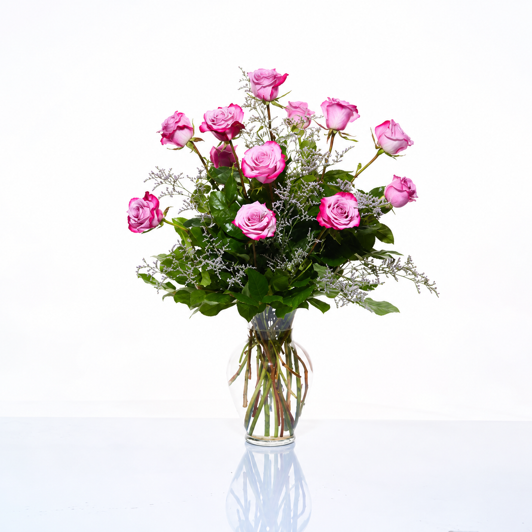 Pink roses arranged at varied heights with greenery in a clear glass vase.
