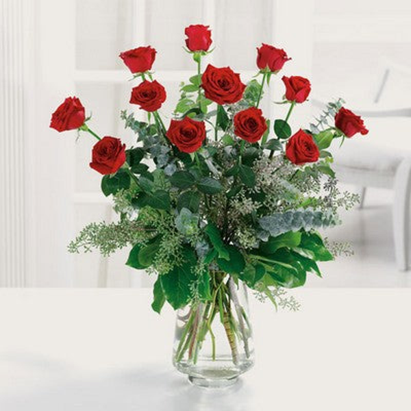 Red roses arranged at varied heights above greenery in a tall clear glass vase.