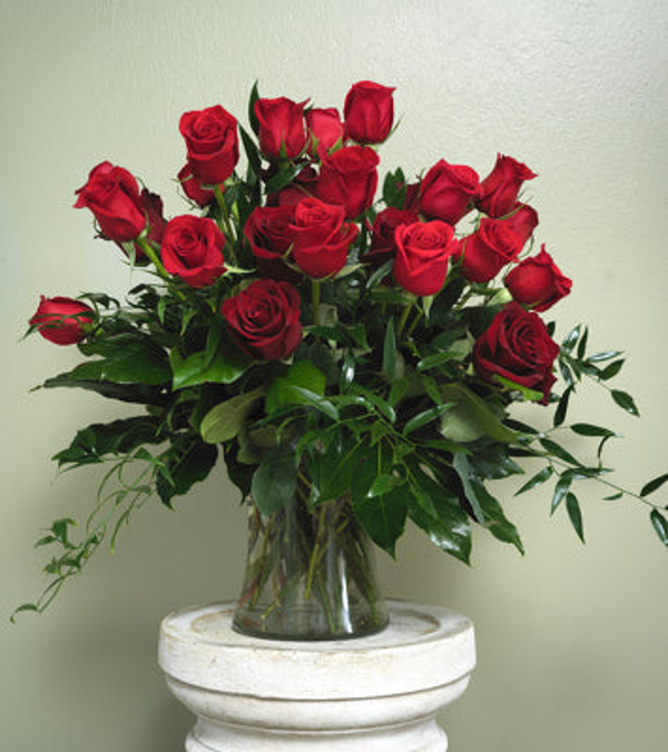 Red roses arranged at varied heights above spreading greenery in a clear glass vase.