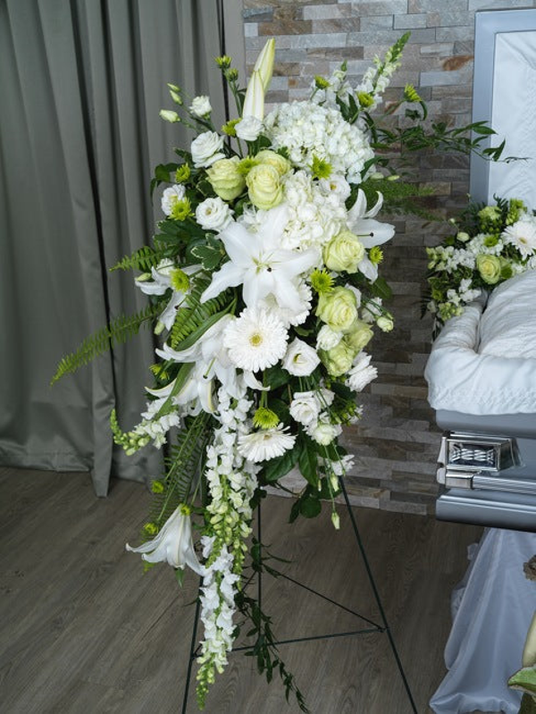 White lilies, hydrangeas, chrysanthemums, and pale green roses with trailing white flowers and ferns in a standing easel spray.